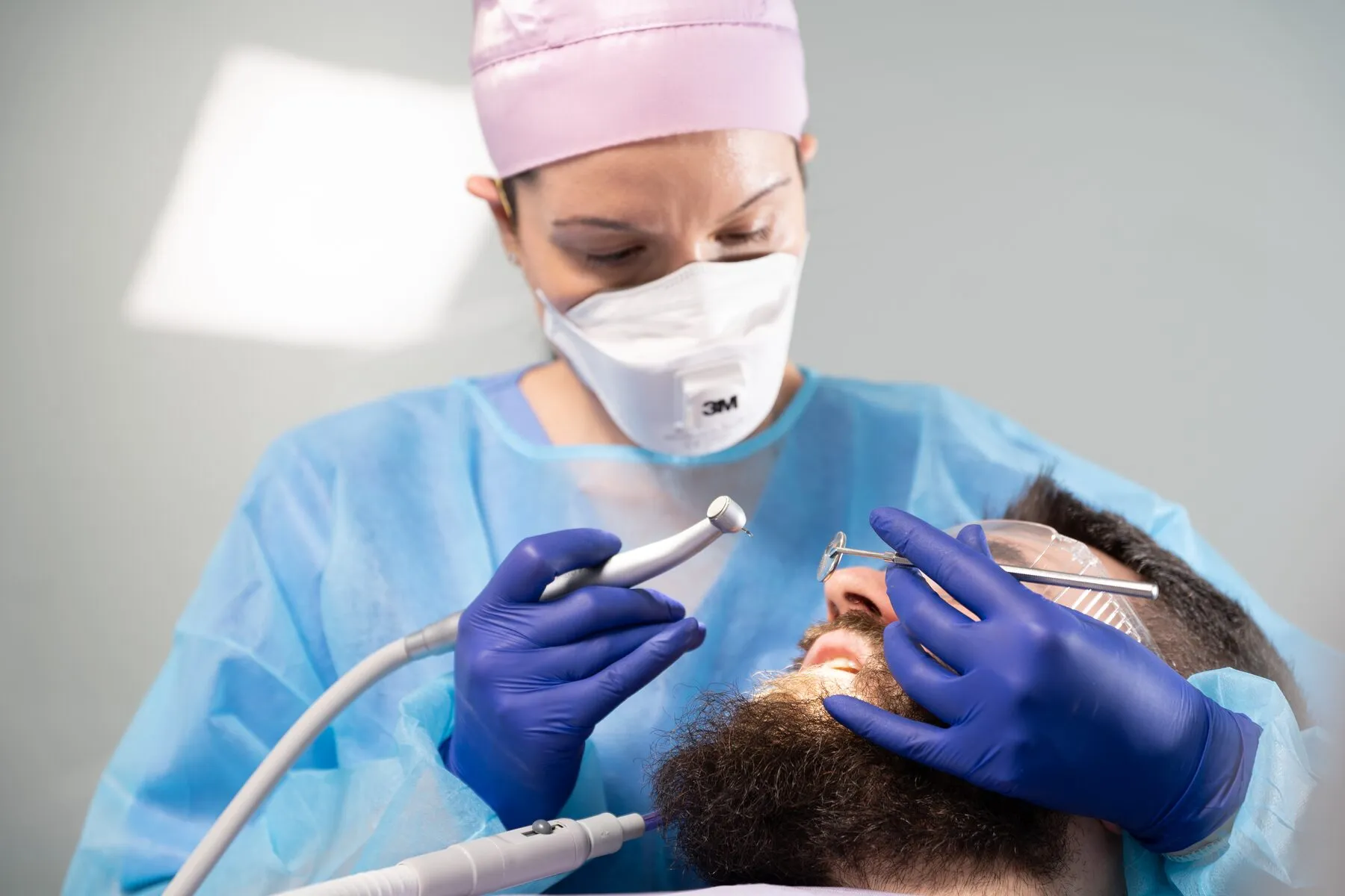 Dr. Roxana Usturoi, cu mască și halat de protecție, tratează un pacient care poartă ochelari de protecție